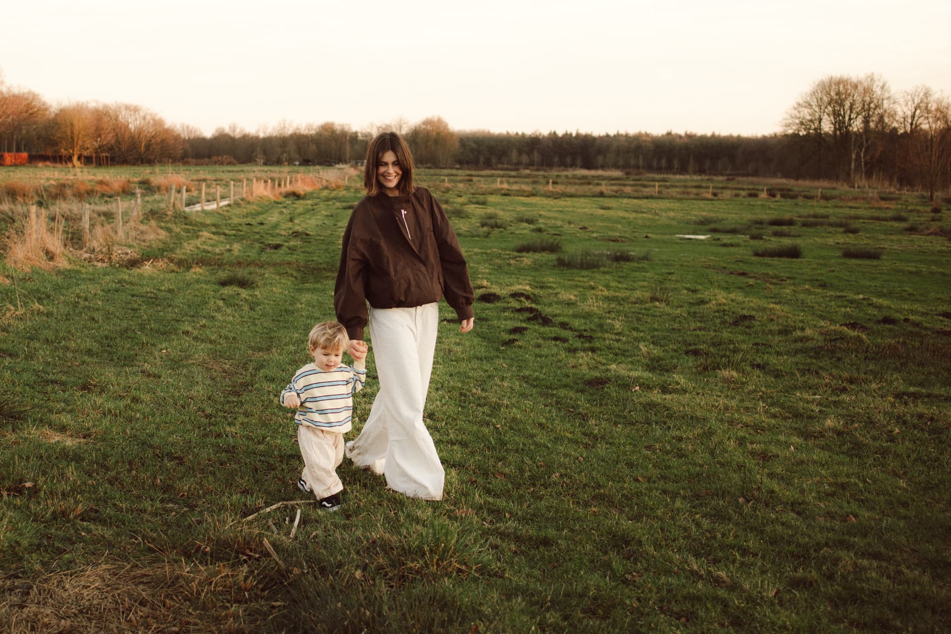 Moeder en kind lopen hand in hand door een groen veld tijdens de gouden uur