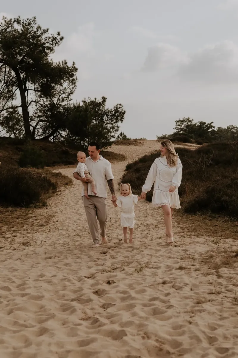 Gezin wandelt over een zandpad tussen heide en duinen.