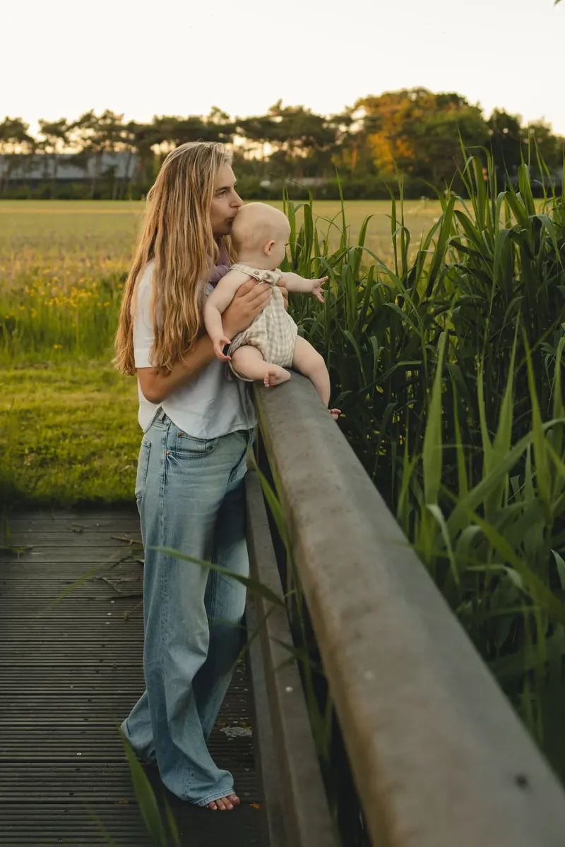 Moeder met baby op een houten bruggetje in het groen.