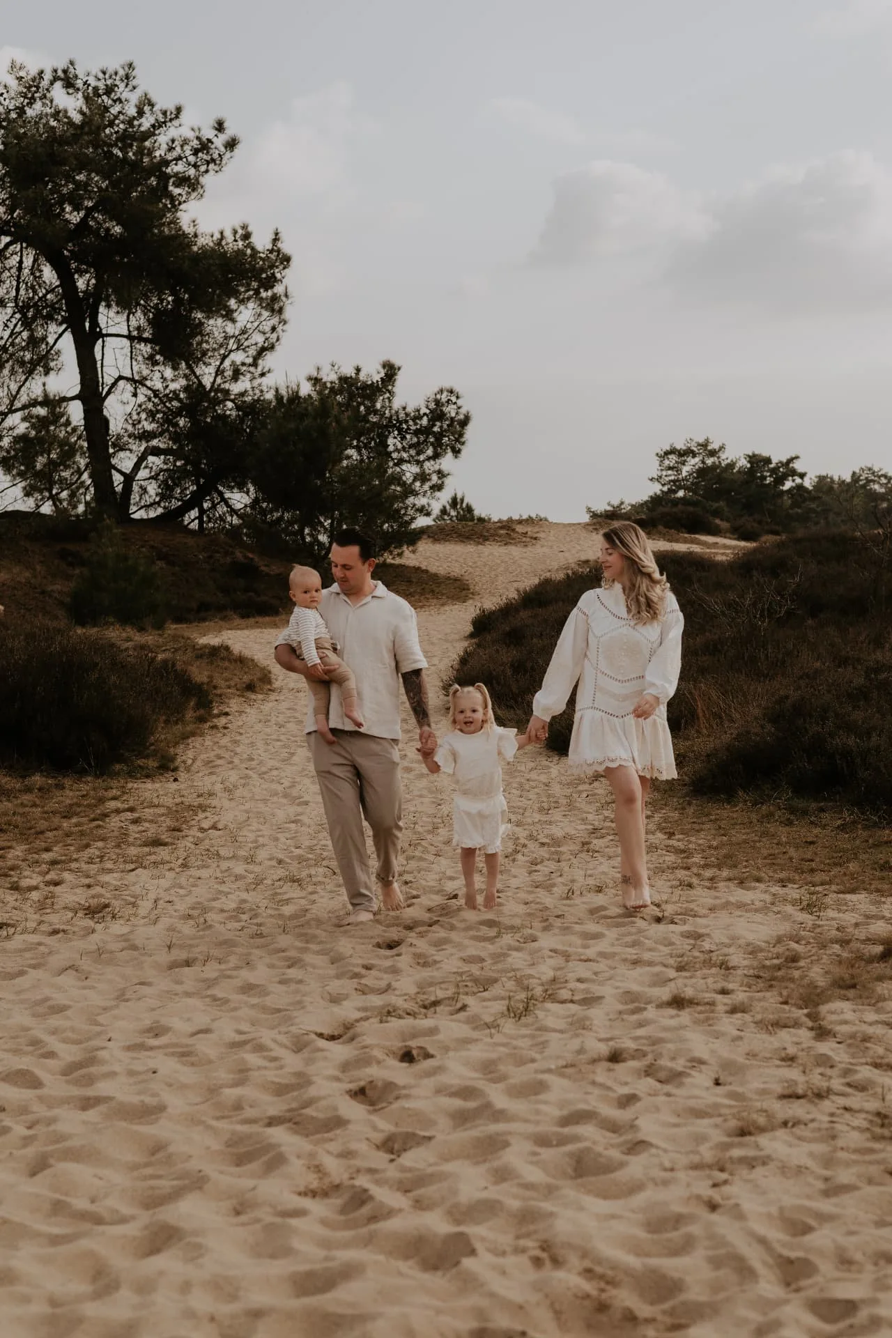 Gezin wandelt over een open zandpad tussen heide en duinen
